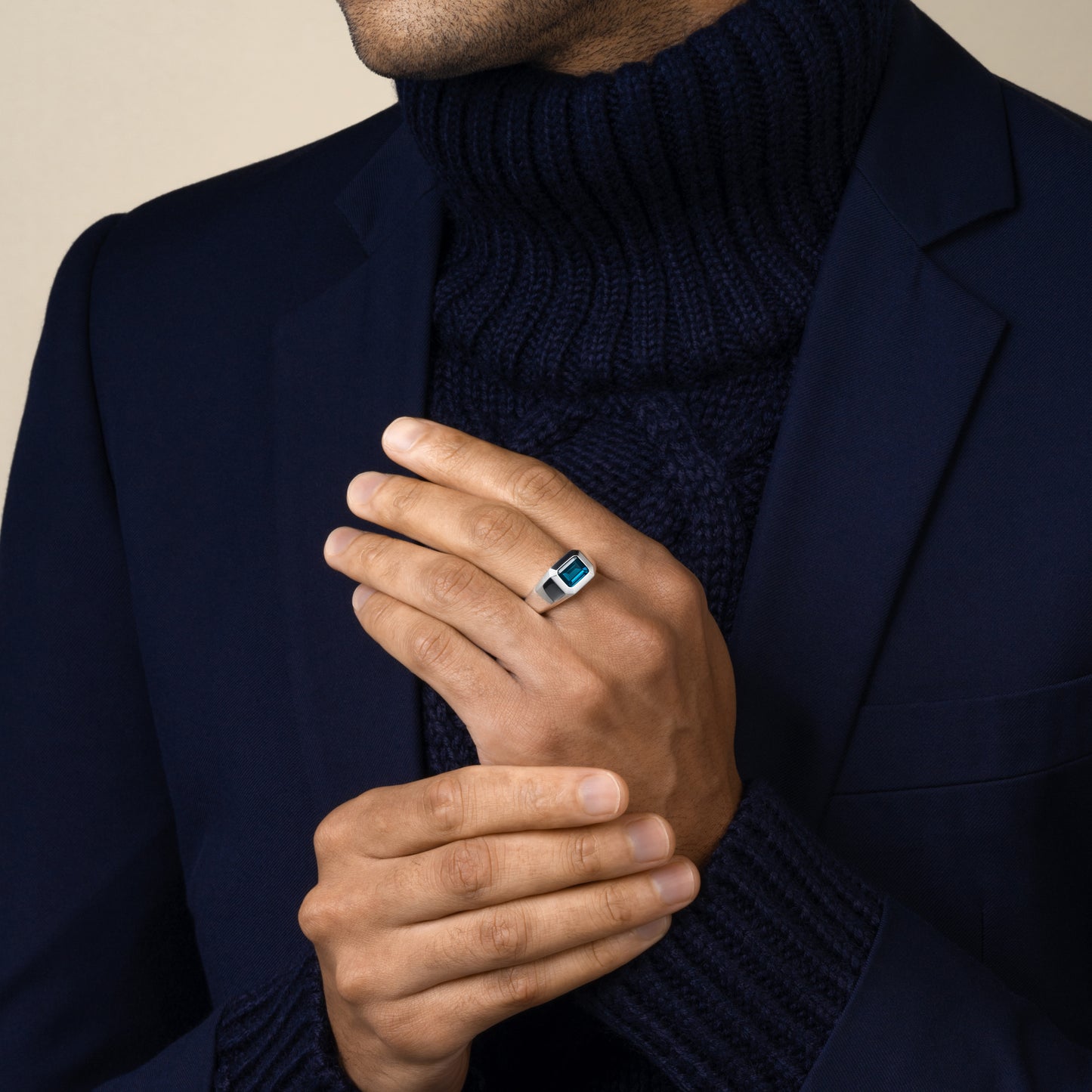 Man wearing a dark blue turtleneck and navy suit blazer with a sterling silver london blue topaz ring on his hand