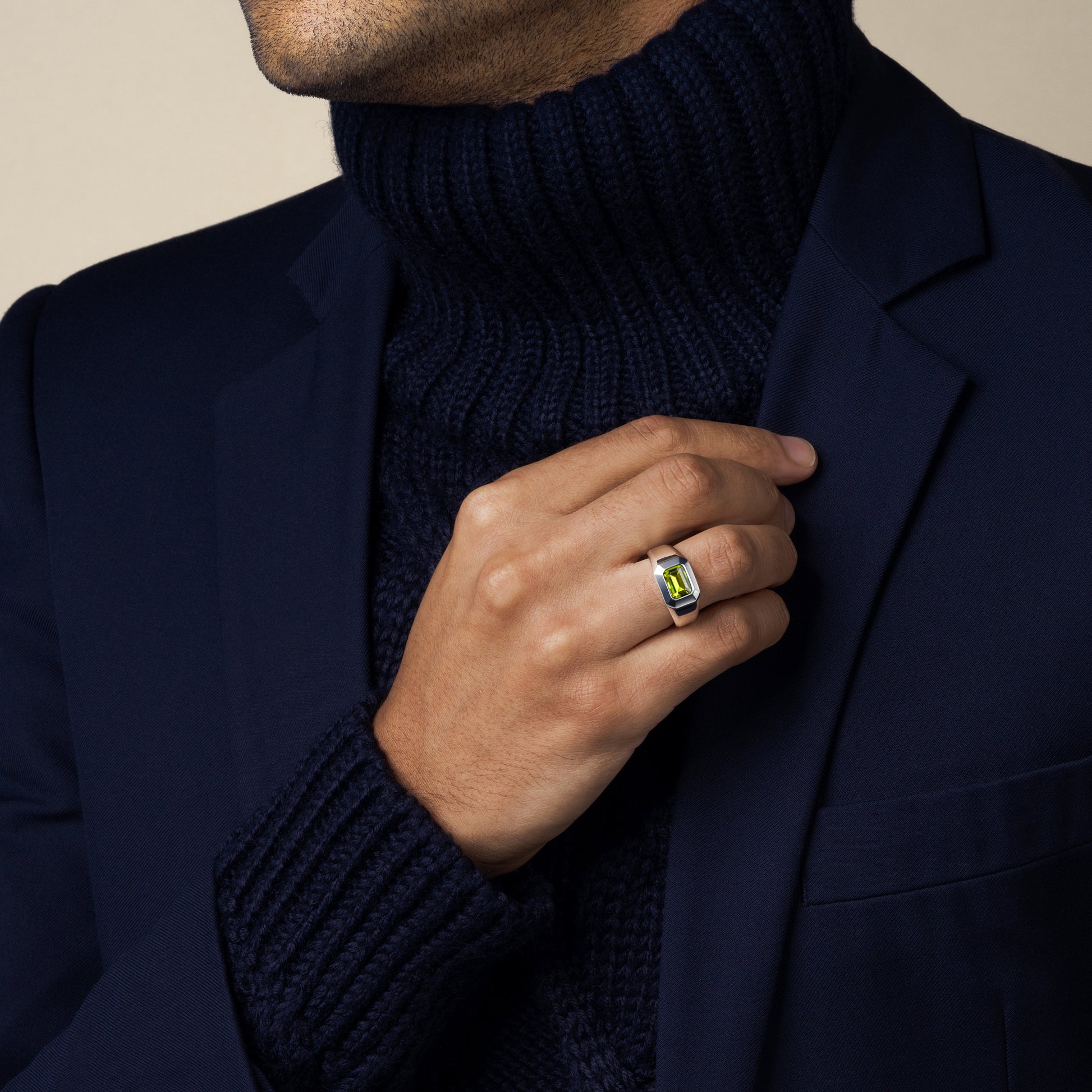 Man wearing a dark blue turtleneck sweater and navy blazer with a sterling silver peridot ring on his hand