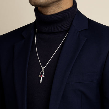 A model wearing a navy blue blazer and turtleneck, modelling a silver ancient Egyptian ankh pendant necklace featuring a round red ruby cabochon stone.